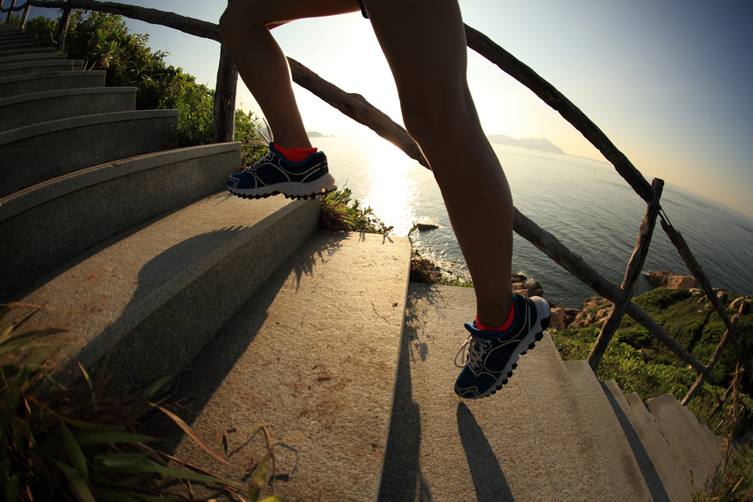 fitness woman runner legs running on seaside mountain stairs, training for trail running.